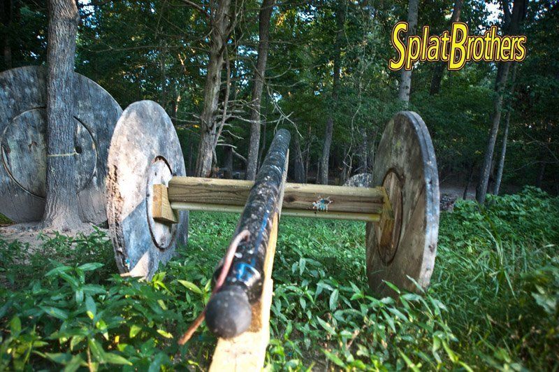 A person is standing on a wooden plank in a paintball field.