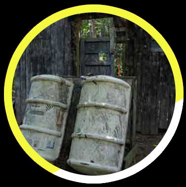 Two barrels are sitting in front of a wooden fence.