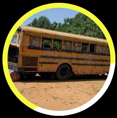 An old yellow school bus is parked in a dirt field.