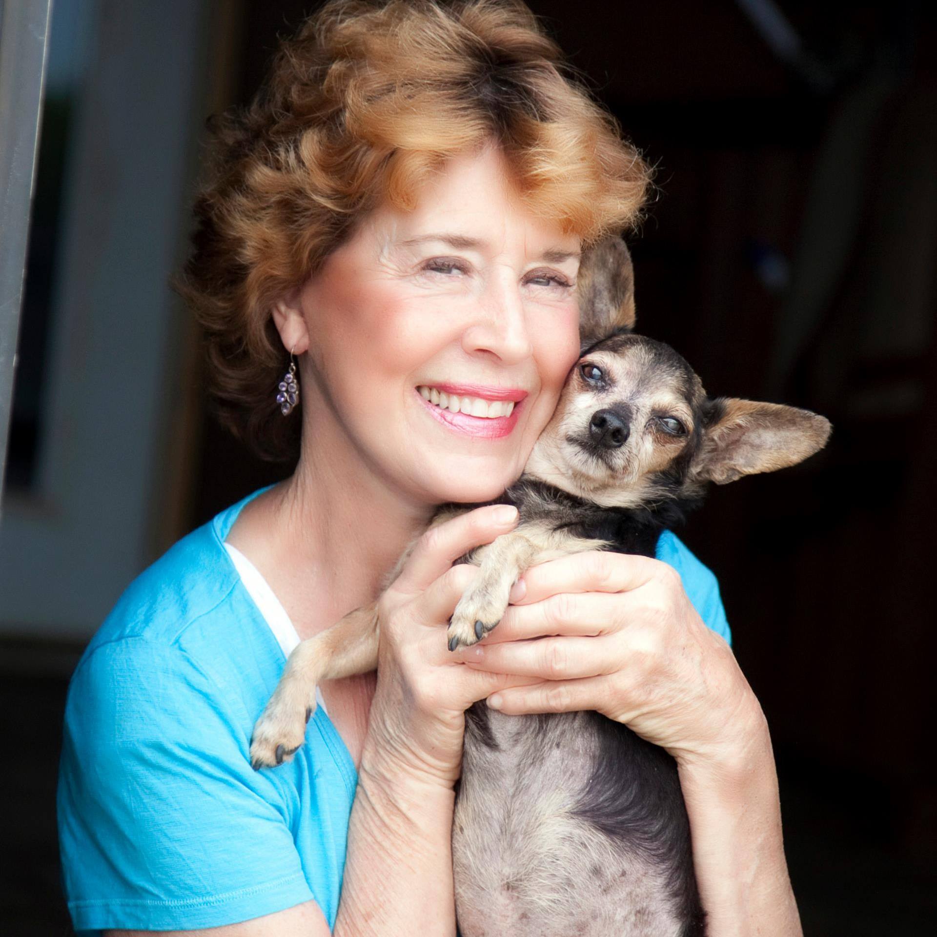 Woman in blue shirt smiling, holding small dog with dark fur.