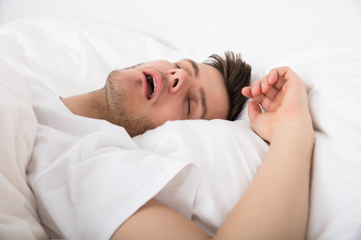 Man sleeping, mouth open, in bed, white sheets, close-up.