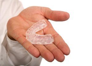 Hand holding a clear, U-shaped mouthguard, likely for dental protection.