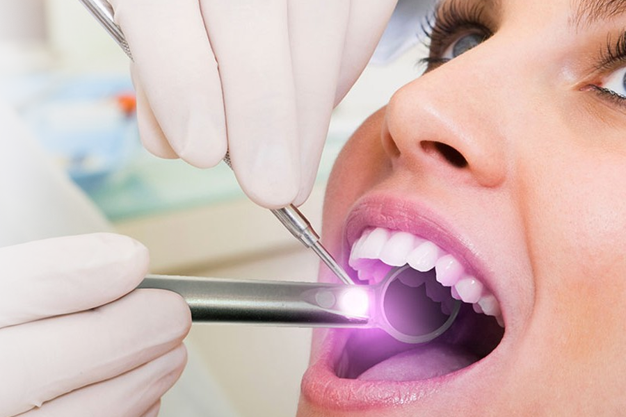 Dentist examining patient's teeth with a mirror and tool in a dental clinic; close-up.