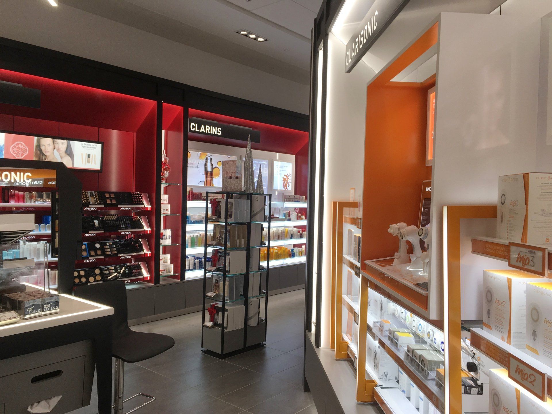 Intérieur d'un magasin de cosmétiques : étagères avec produits et éclairage. Touches de rouge et d'orange.