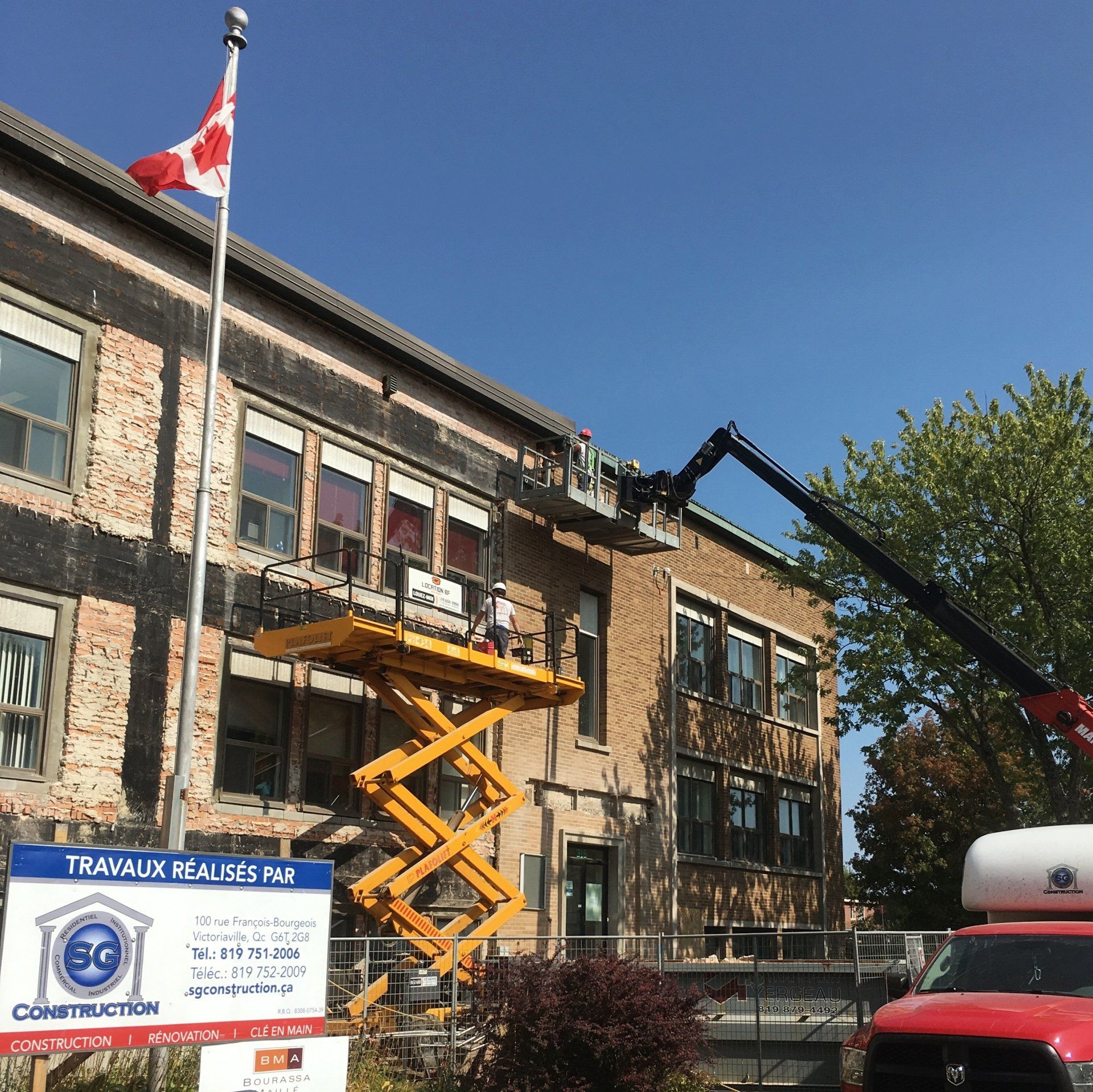 Construction d'un bâtiment en briques arborant un drapeau canadien. Ouvriers sur des plateformes élévatrices.