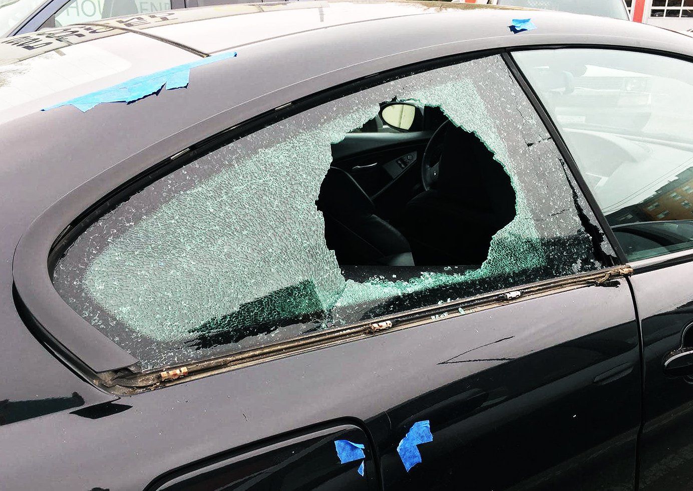 A black car with a broken window and blue tape on it.
