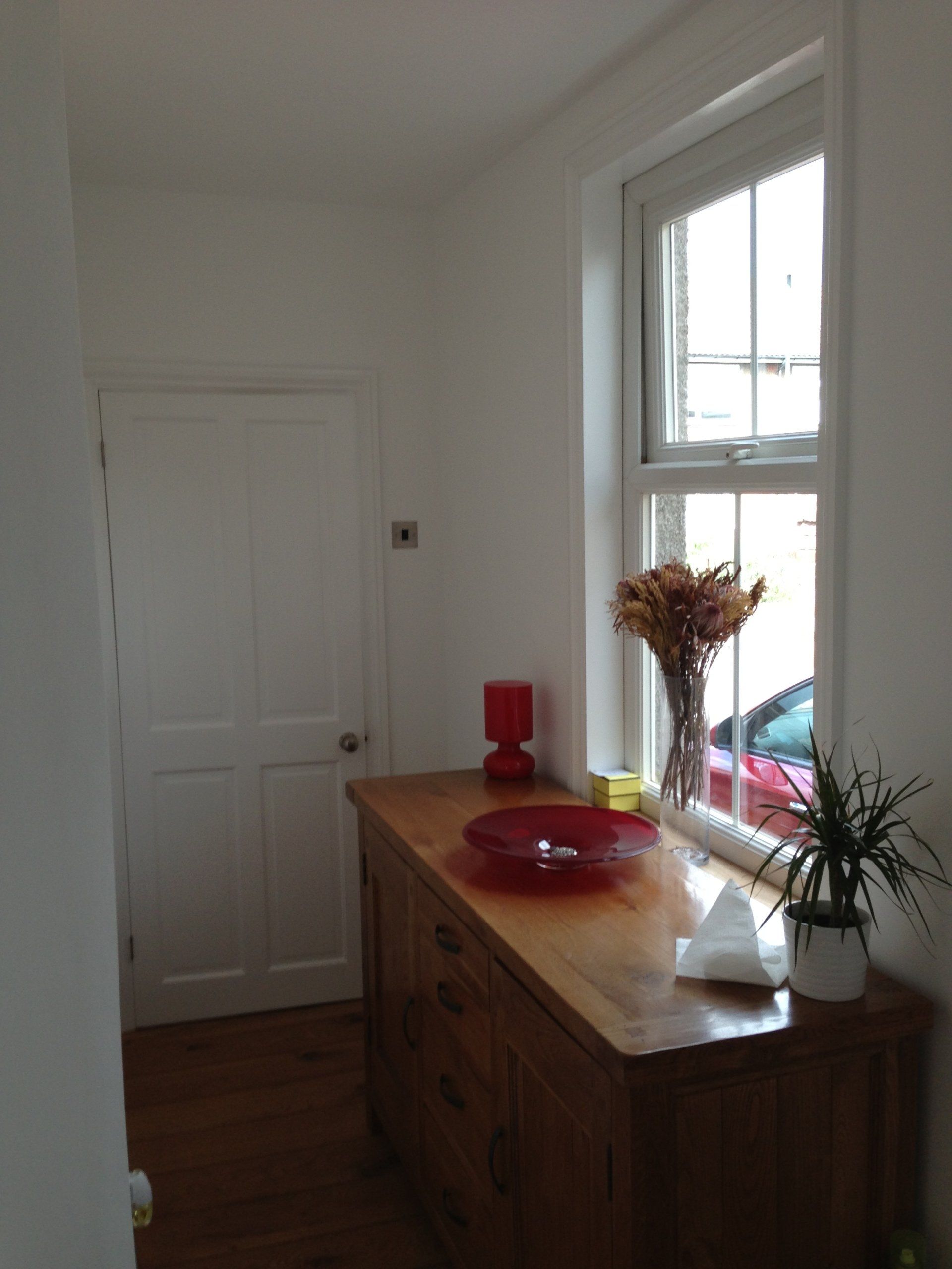 A solid wood sideboard in a hallway in front of window.
