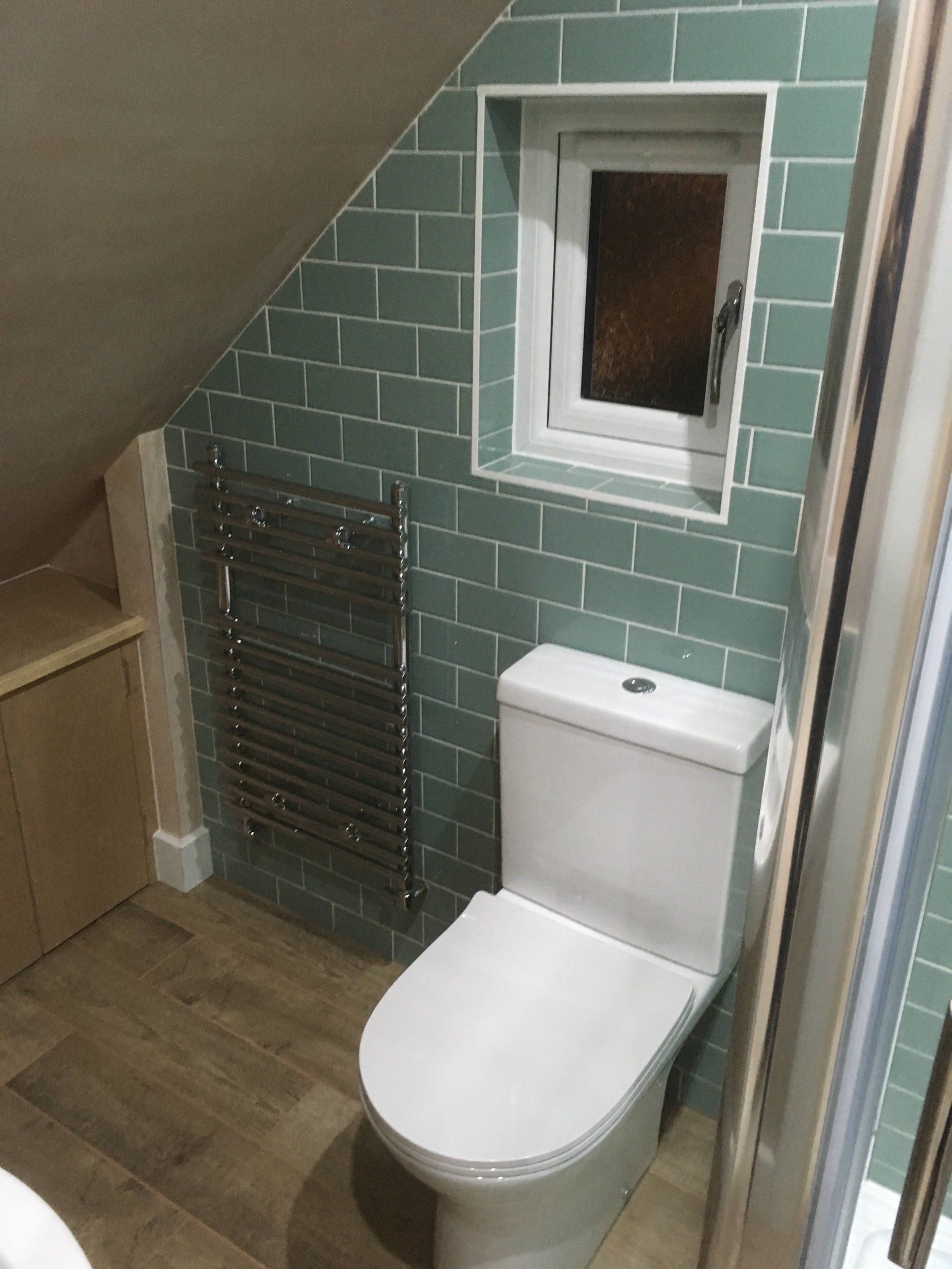A toilet and heated towel rail installed onto a tiled wall.