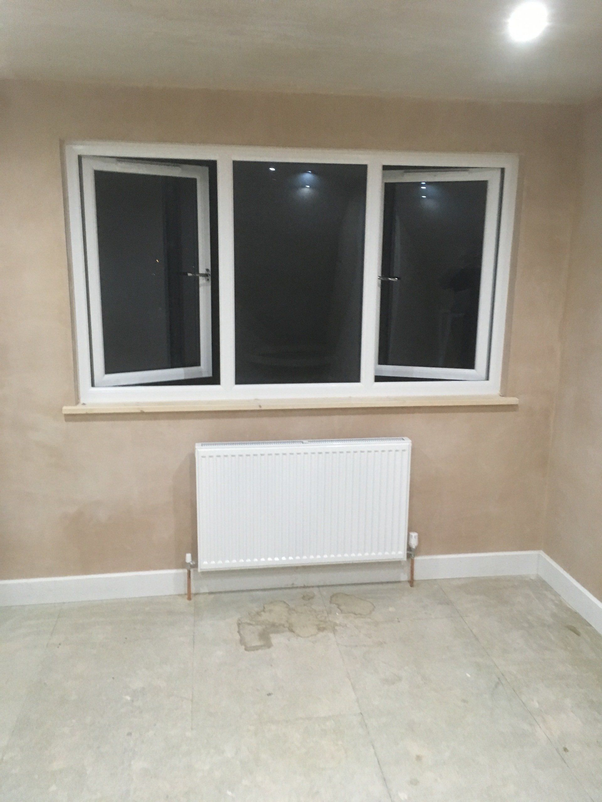 A newly plastered wall behind a small radiator.