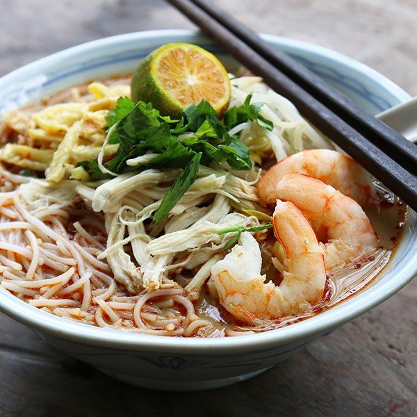 A bowl of noodles and shrimp with chopsticks on a table
