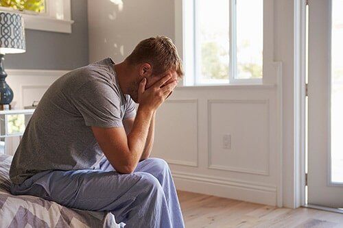Man sitting on bed with hands on face — Psychological Counseling in Bethlehem, PA Man sitting on bed with hands on face — Psychological Counseling in Bethlehem, PA