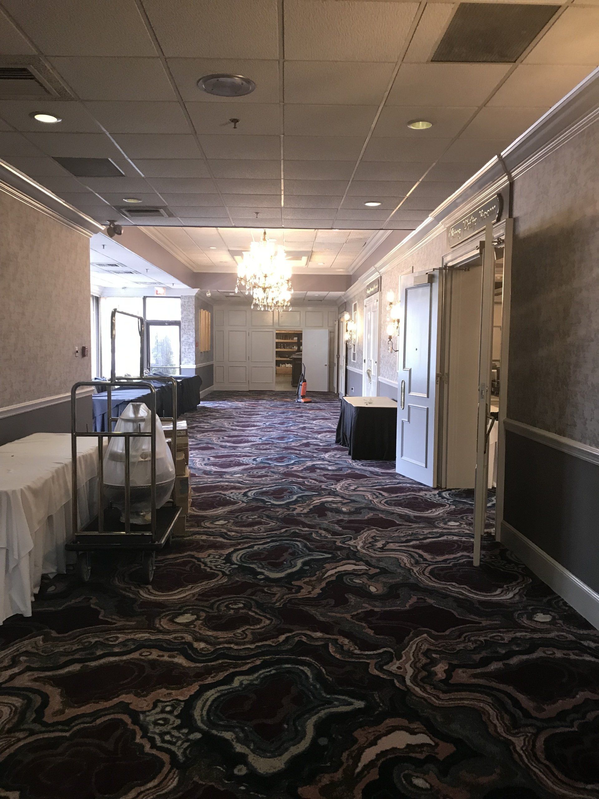 A long hallway with a carpeted floor and a chandelier hanging from the ceiling.