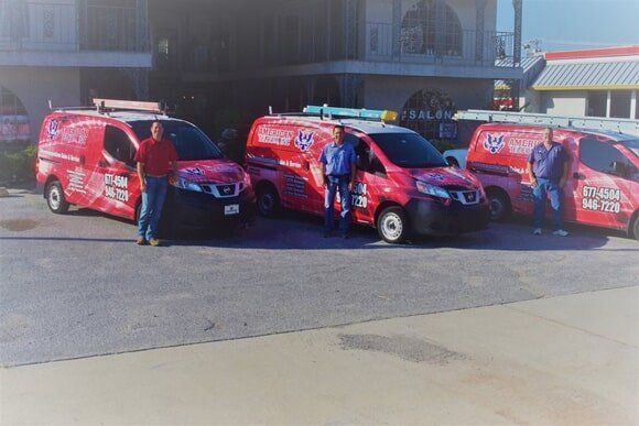 Three red work vans with logos; three men stand with the vans in a parking lot.