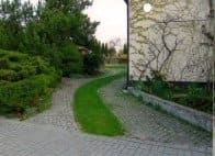 Eine gepflasterte Auffahrt, die zu einem von Bäumen und Büschen umgebenen Haus führt.