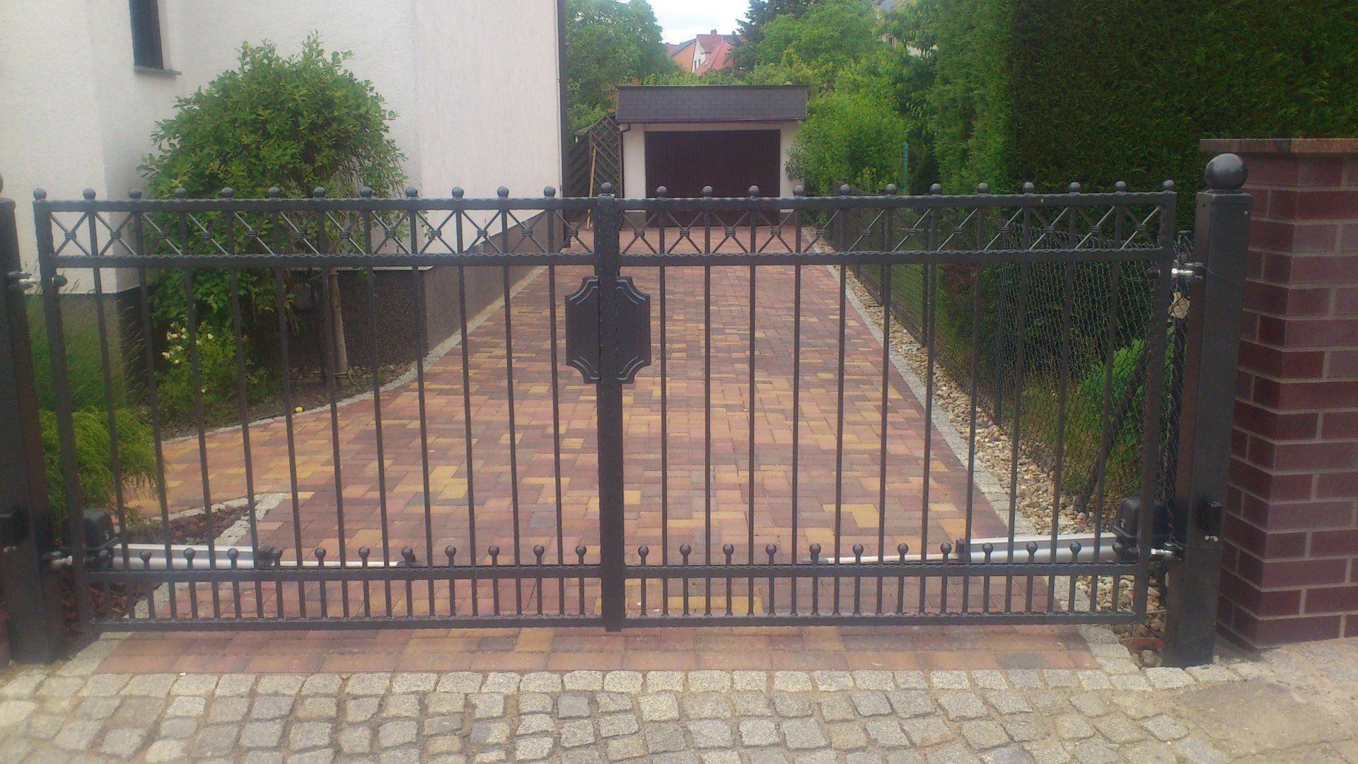 Ein schwarzes schmiedeeisernes Tor führt zu einer gemauerten Auffahrt, die zu einem Haus führt.