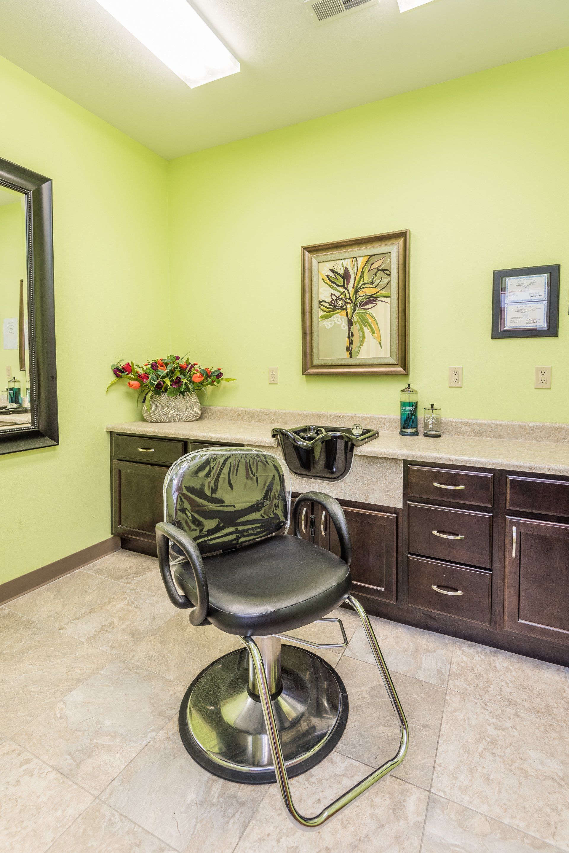 A hair salon with a chair , sink , mirror and cabinets.