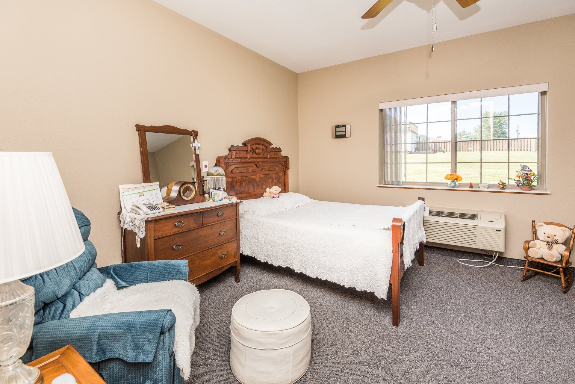 A bedroom with a bed, dresser, chair, lamp and window.