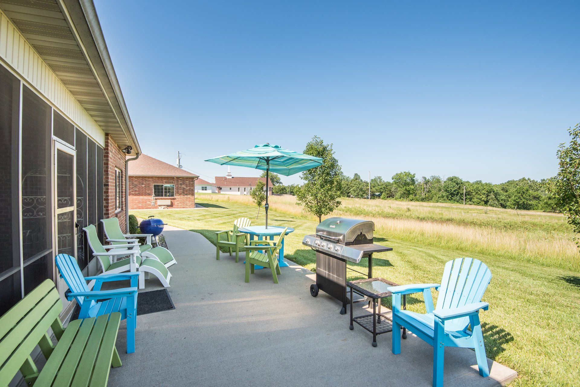A patio with chairs, tables, umbrellas and a grill.