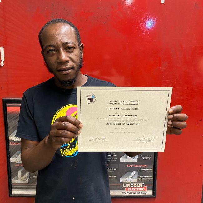Man holding a certificate; standing in front of a red wall.