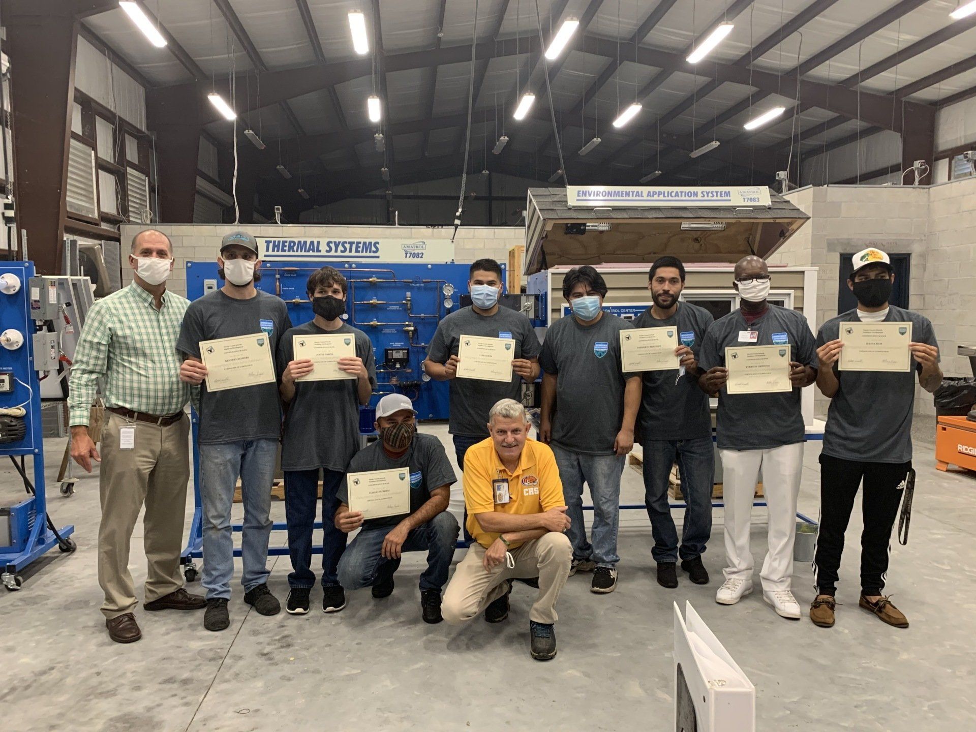 Group of people holding certificates, in a workshop setting. They are wearing masks.