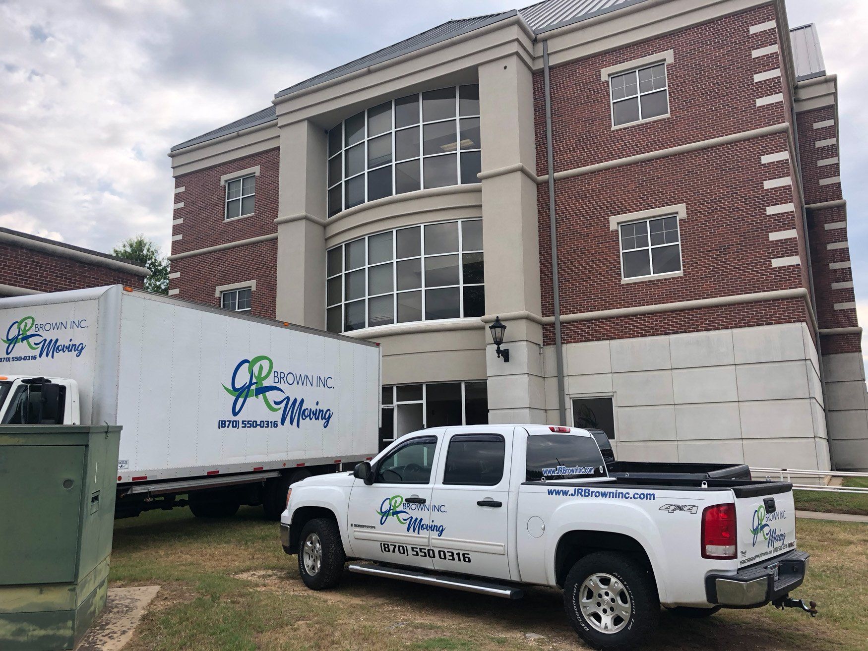 Two white trucks are parked in front of a large brick building.