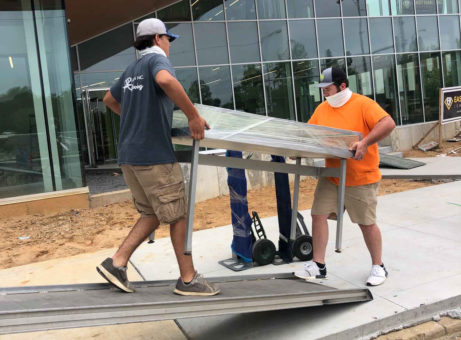 Two men are carrying a large piece of metal on a dolly.