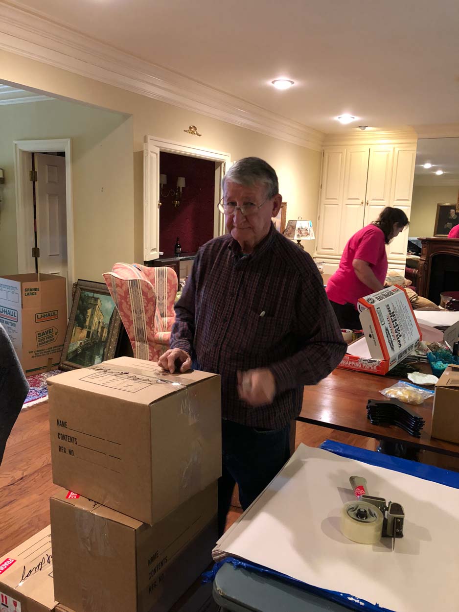 A man is standing next to a pile of cardboard boxes in a living room.