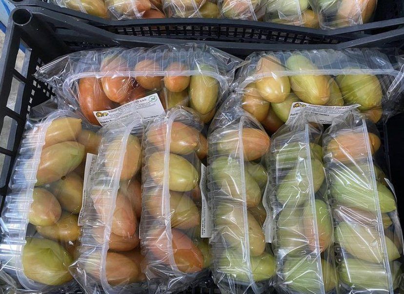 Cassette di plastica piene di prodotti ortofrutticoli giallo-verdi e arancioni confezionati in sacchetti, esposte su una bancarella del mercato.