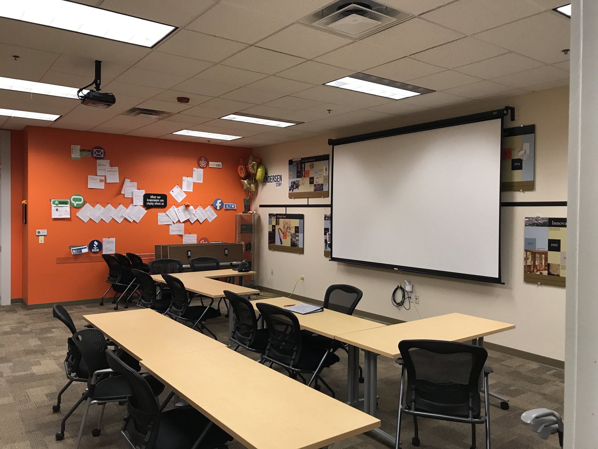 A classroom with tables and chairs and a large screen