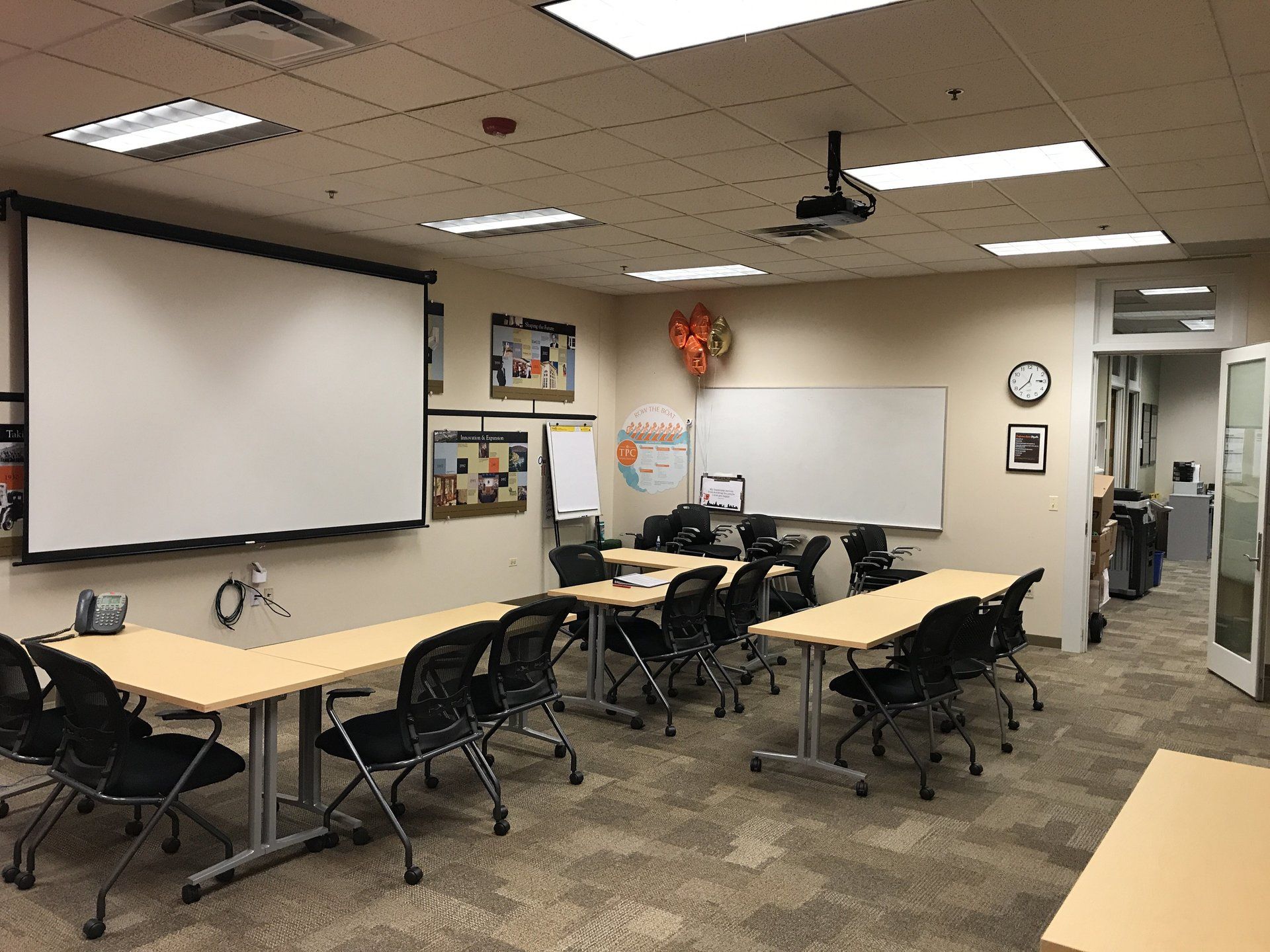 A classroom with tables and chairs and a projector screen.