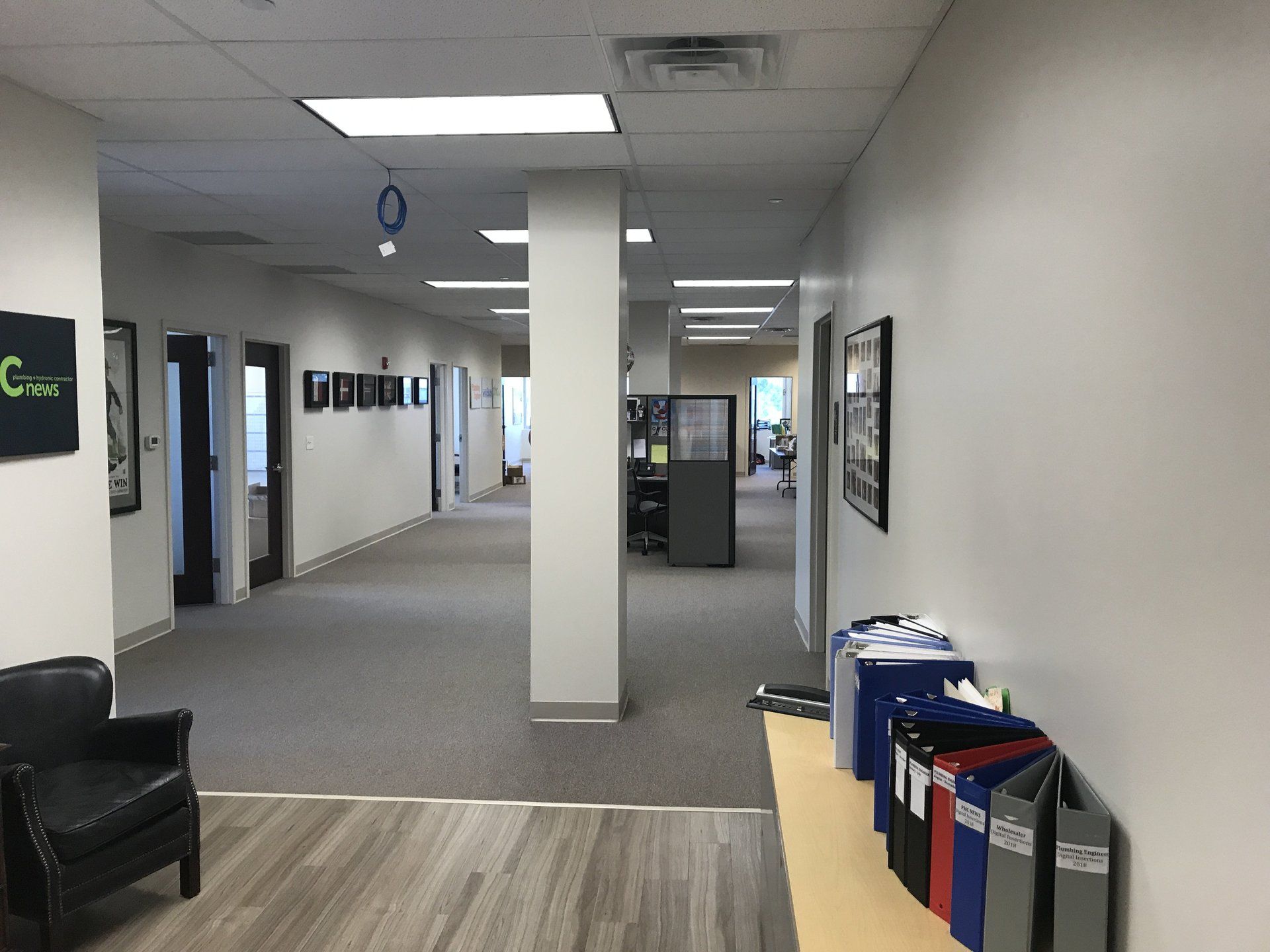 A long hallway in an office building with a chair and binders on the floor.