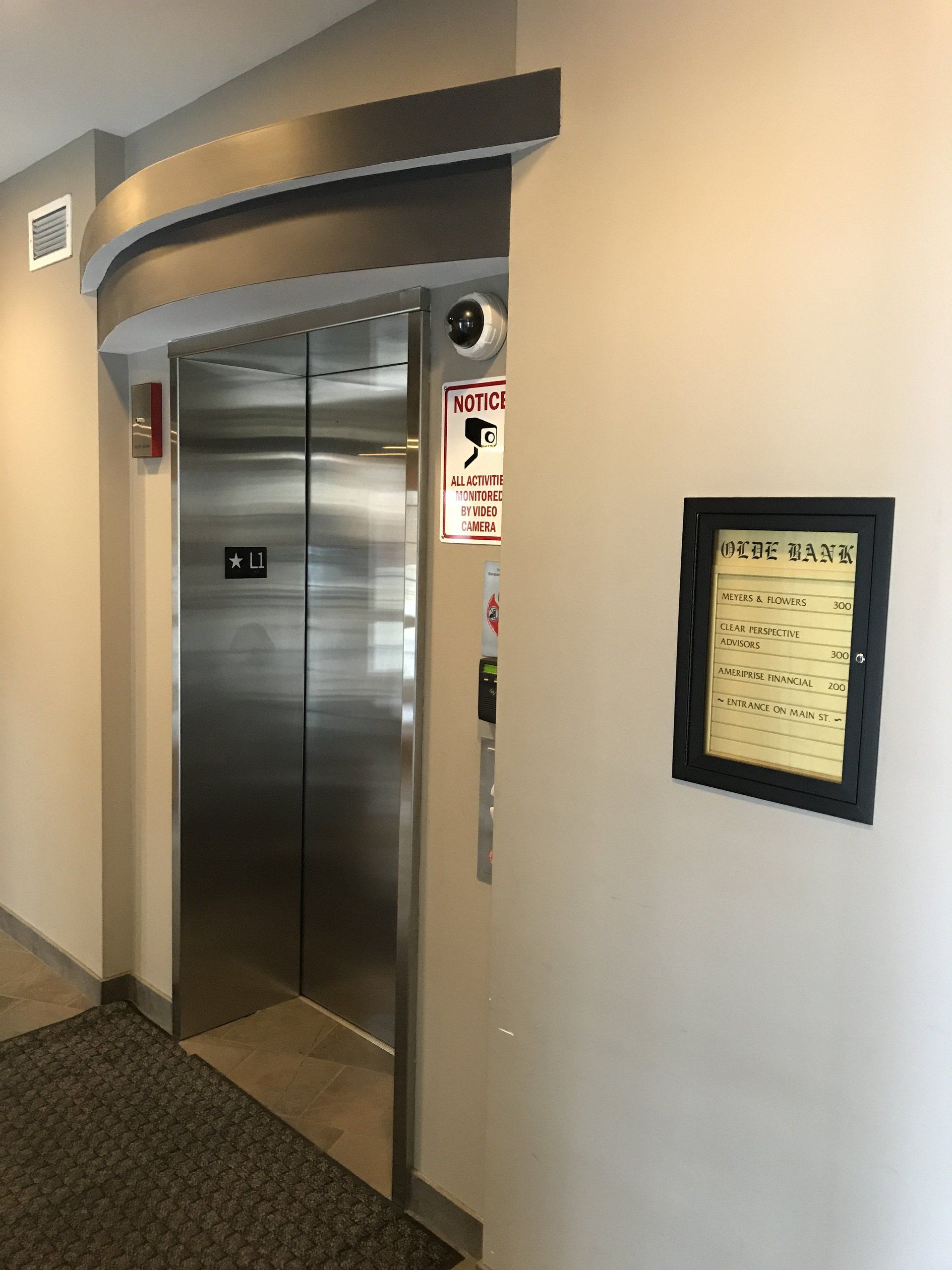 A stainless steel elevator is sitting in a hallway next to a bulletin board.