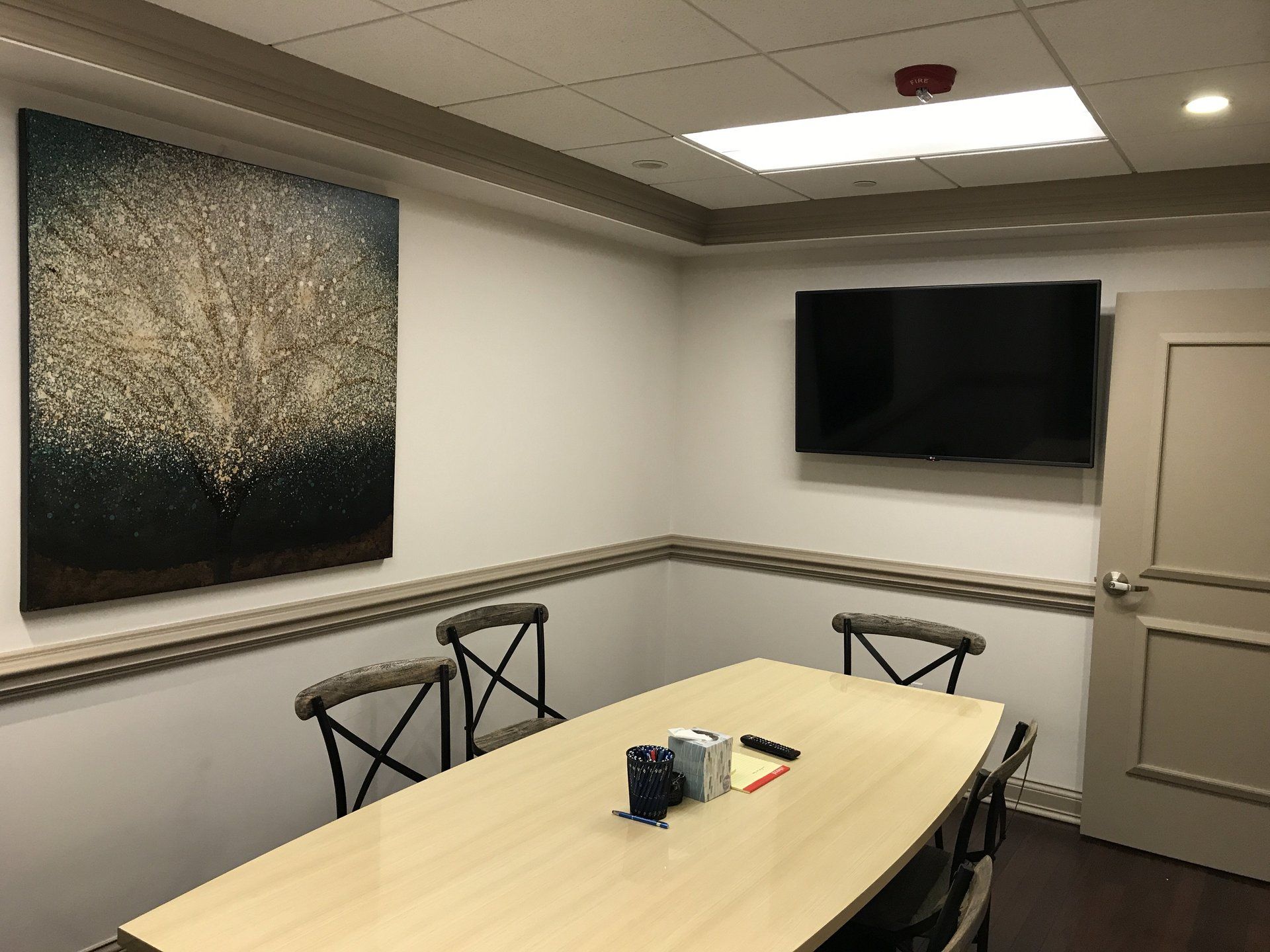 A conference room with a table and chairs and a television on the wall.