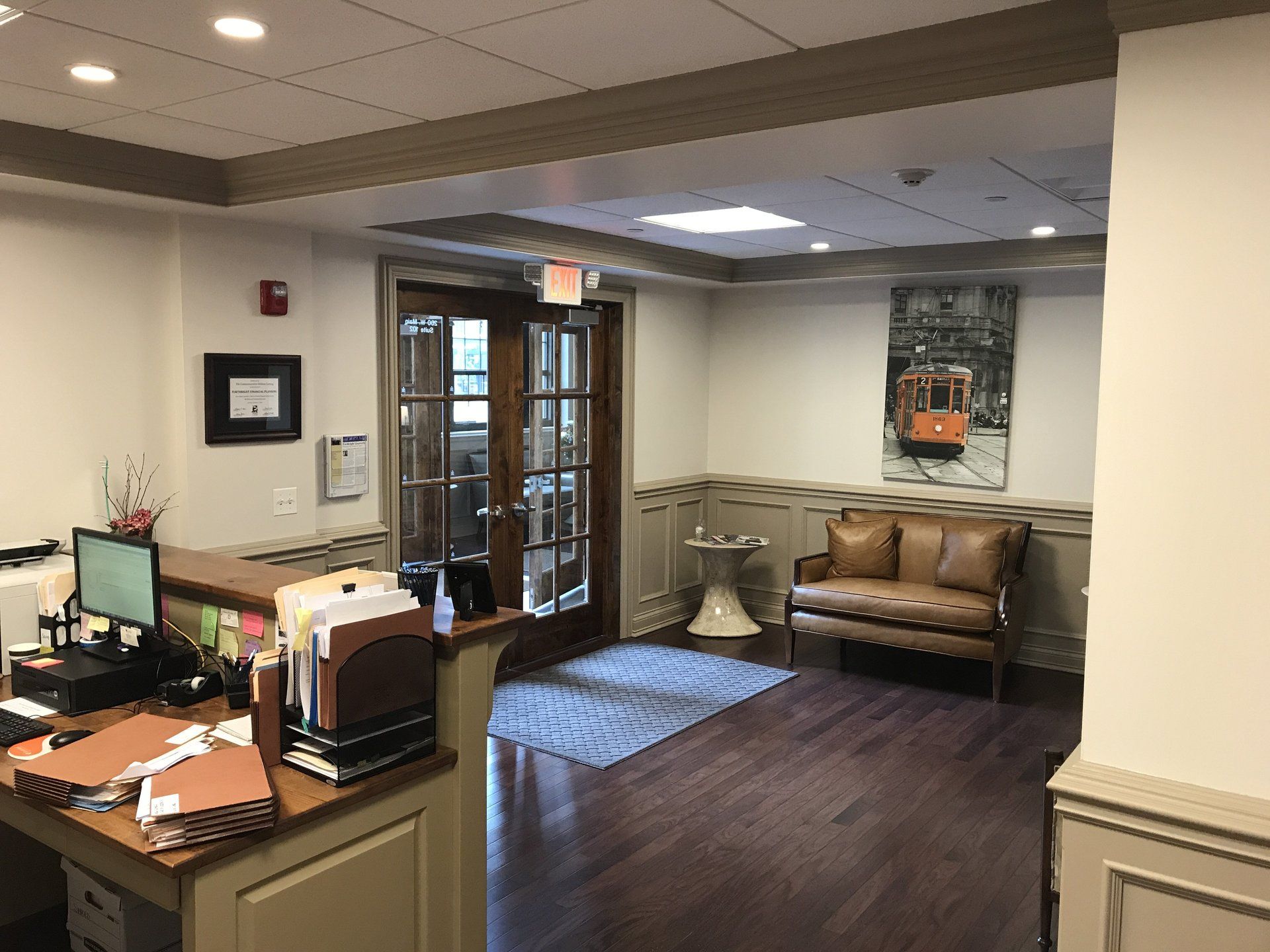 A lobby with a couch , desk , computer and a painting on the wall.