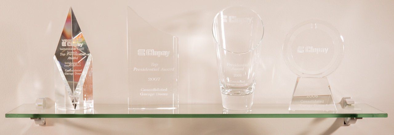 A glass shelf filled with trophies and glasses on a wall.