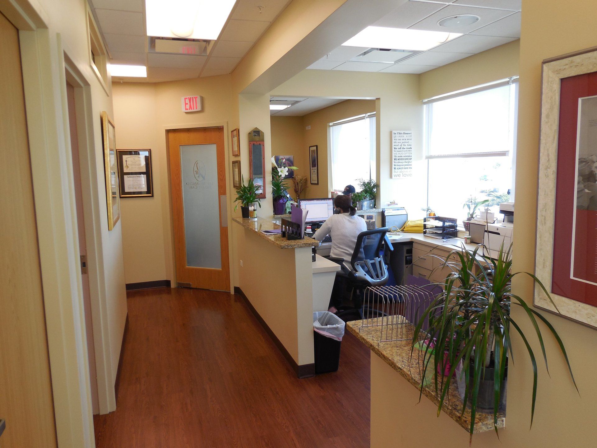 A woman is sitting at a desk in a hallway in a dental office.