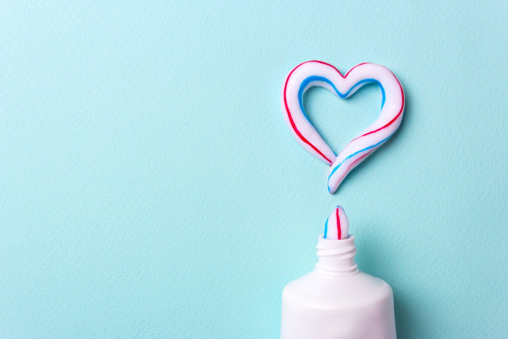 A tube of toothpaste with a heart shaped toothpaste coming out of it.