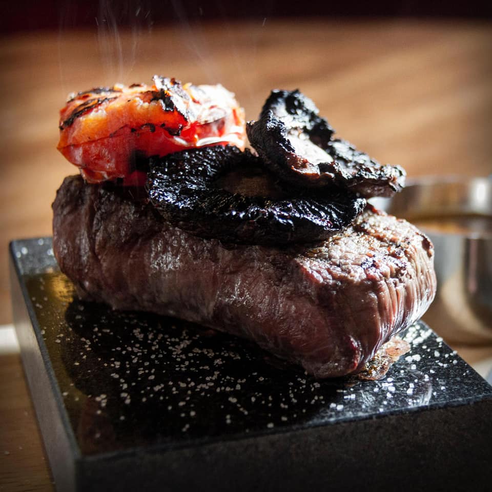 Grilled steak topped with a tomato and charred garnish on a black plate