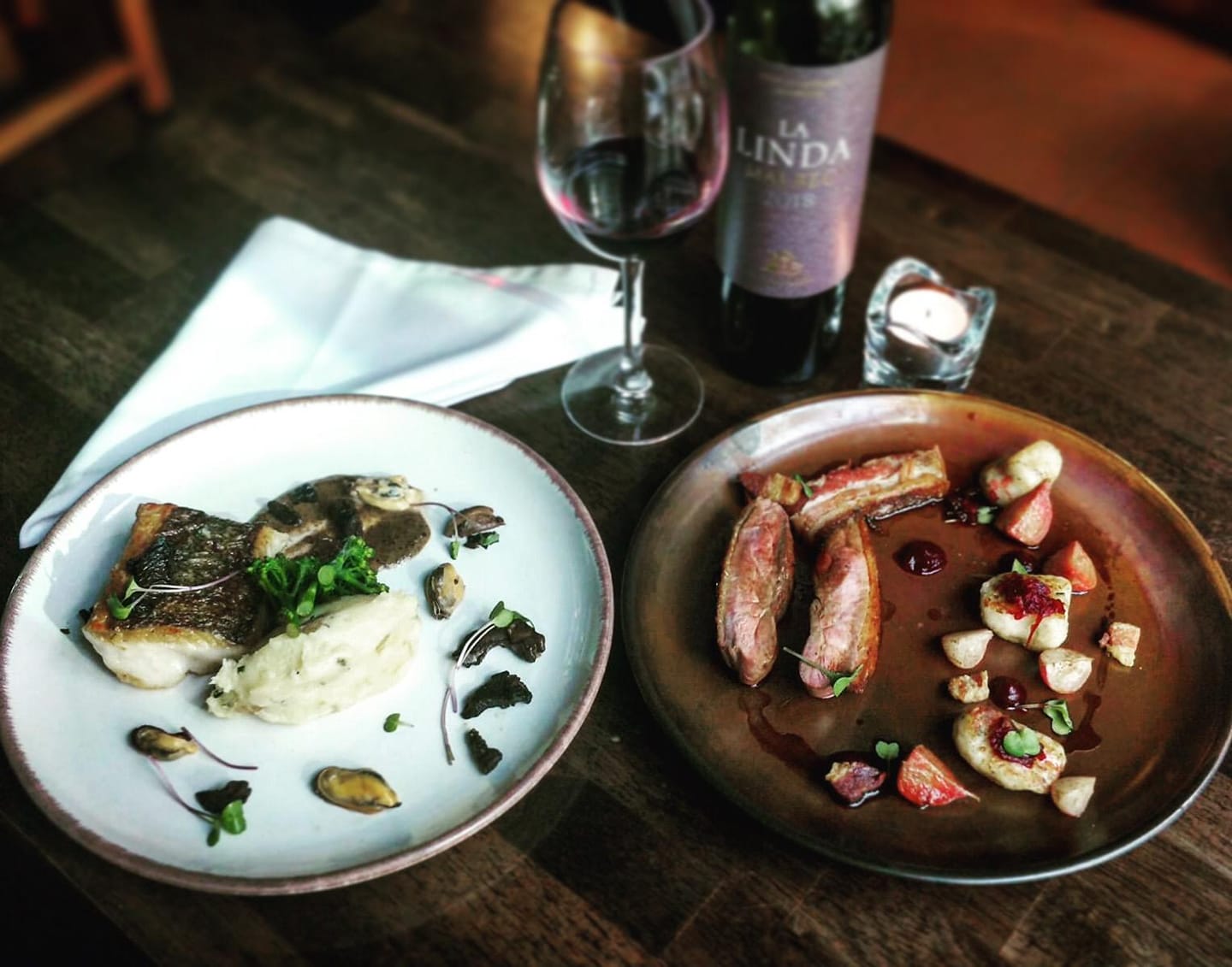 Wine and plated gourmet dishes on a restaurant table, with candlelight ambiance.