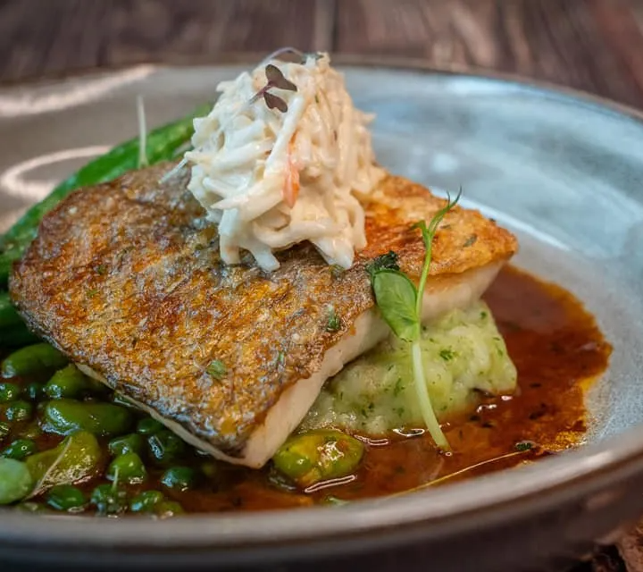 Pan-seared fish with herbs and crab garnish over mashed potatoes and sauce on a gray plate