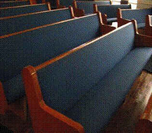Rows of blue cushioned church pews with wooden armrests.