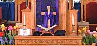 A church altar with a cross, open book, candles, and flowers, draped in purple.