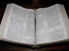 Open Bible on a wooden surface, pages filled with text.