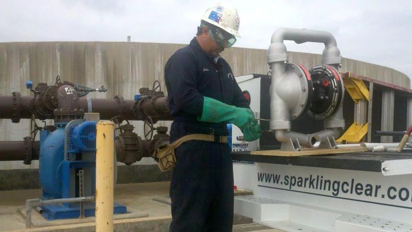 A man wearing a hard hat and green gloves is working on a pump