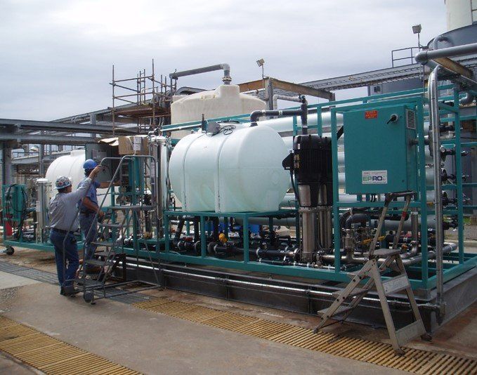 Two men are working on a large tank in a factory