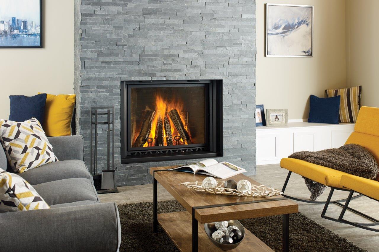 Cozy living room with a lit fireplace set in a stone wall, gray sofa, yellow chair, and wooden coffee table.