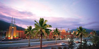 Sunset view of buildings with palm trees and a road in the foreground.