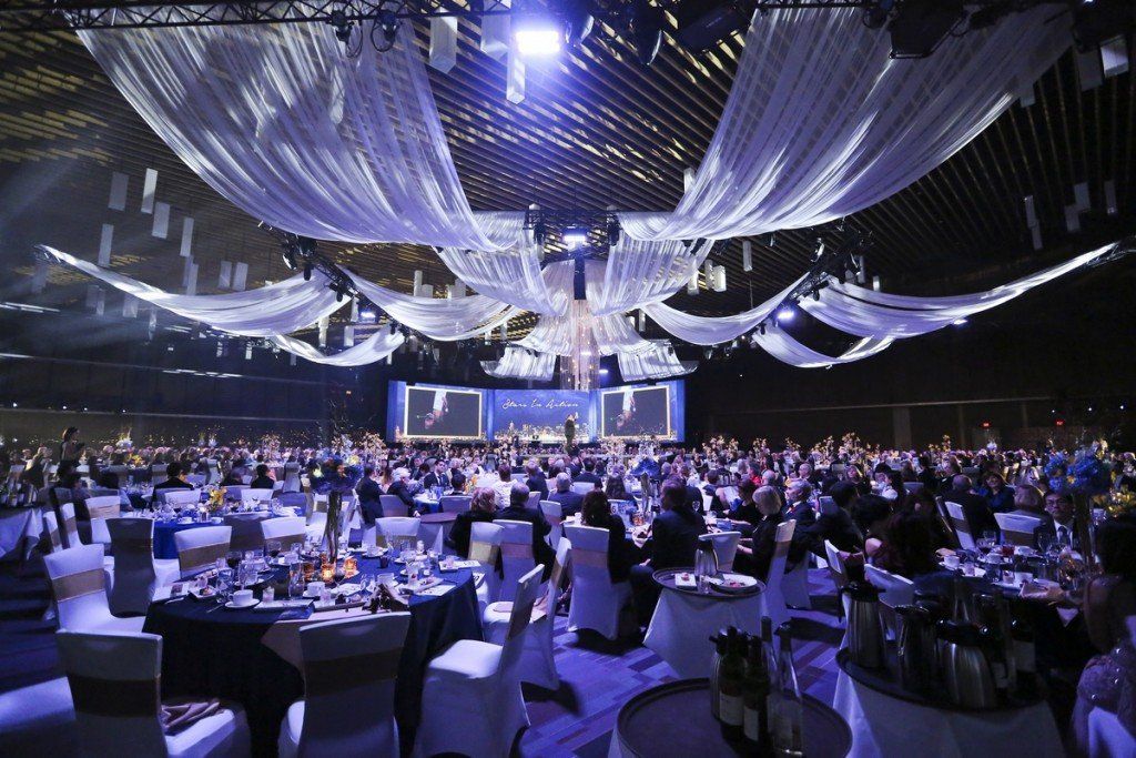 A large crowd of people are sitting at tables in a large room.
