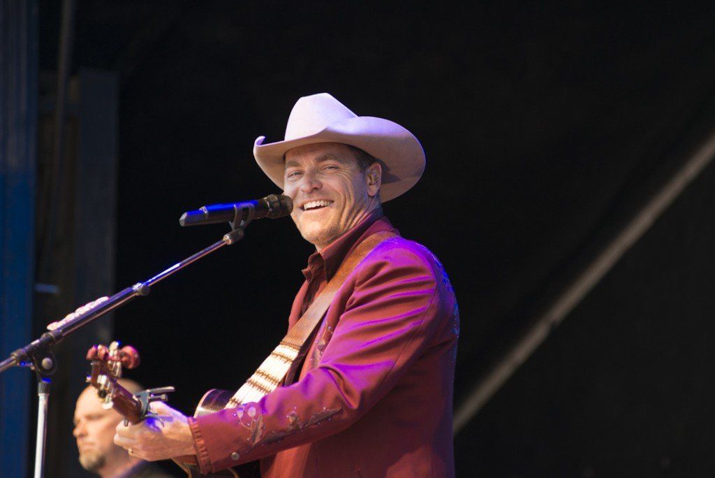 A man in a cowboy hat is singing into a microphone while playing a guitar.