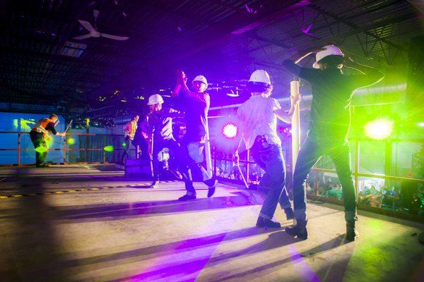 A group of people wearing hard hats are dancing on a stage.